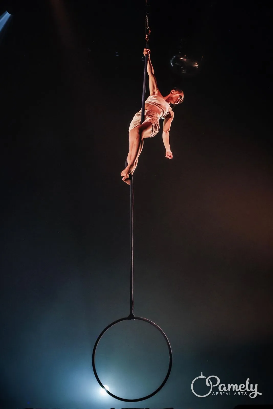 Pamely climbing the rope above her hoop on a dark stage