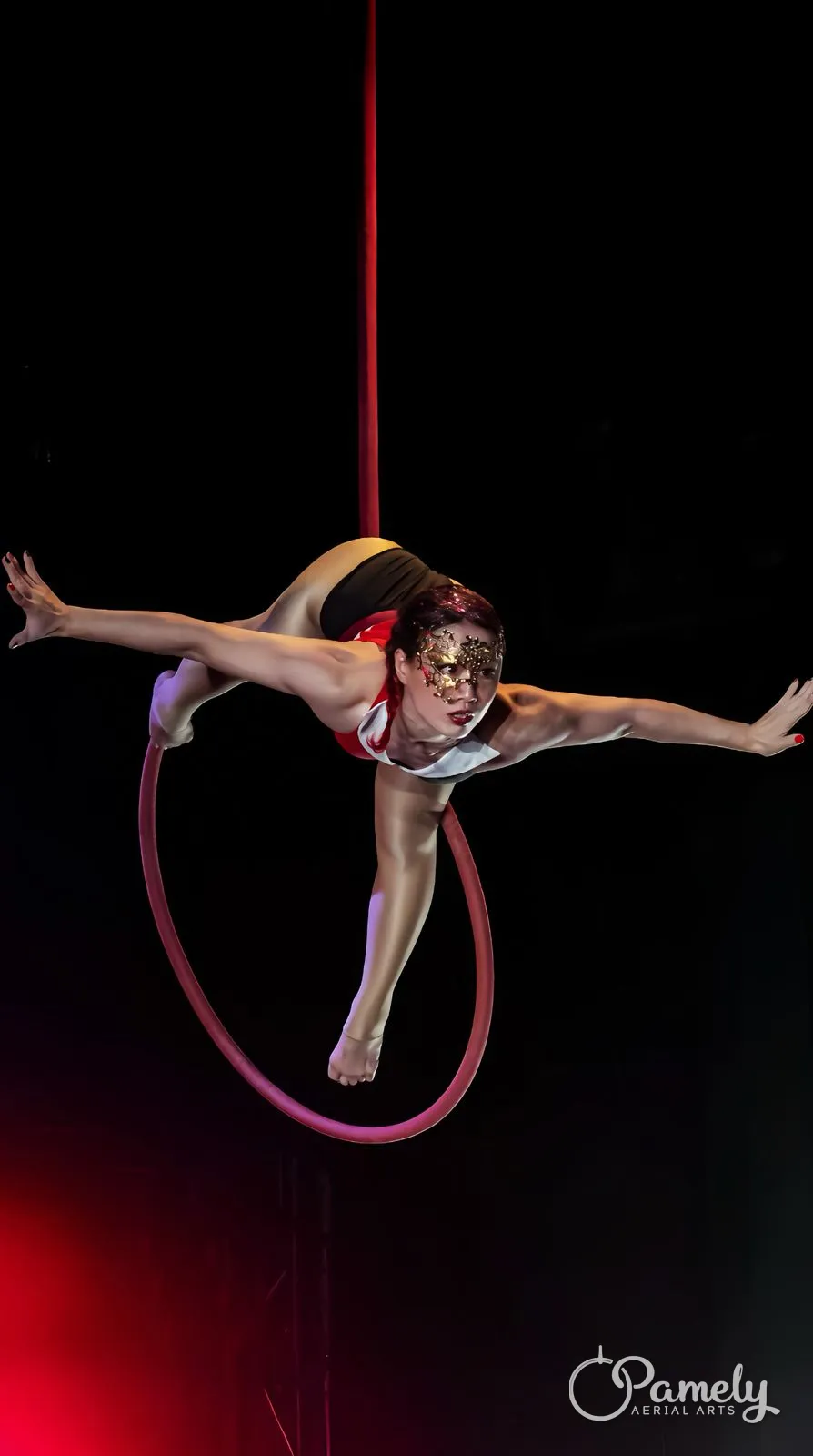 Pamely in an arabesque inside the hoop under red stage light
