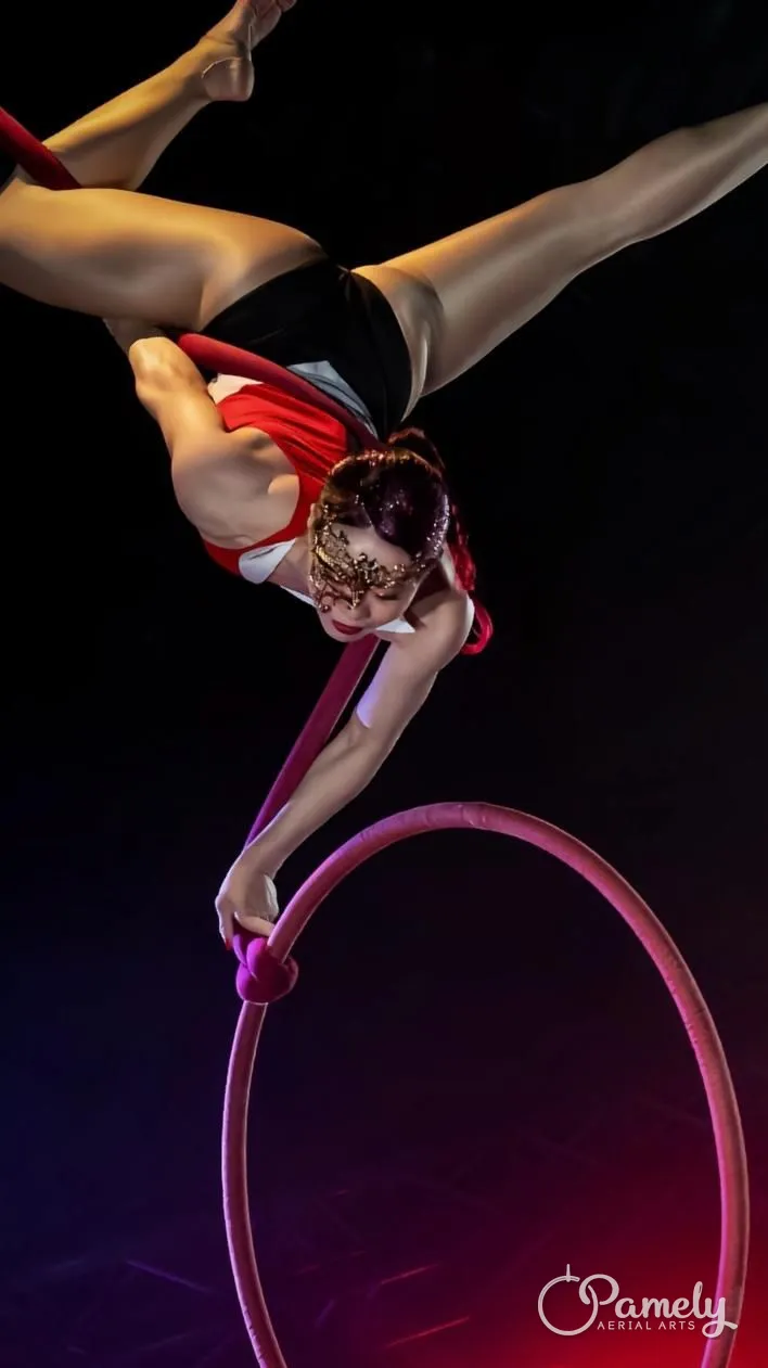 Pamely in a split above the hoop on a dark stage
