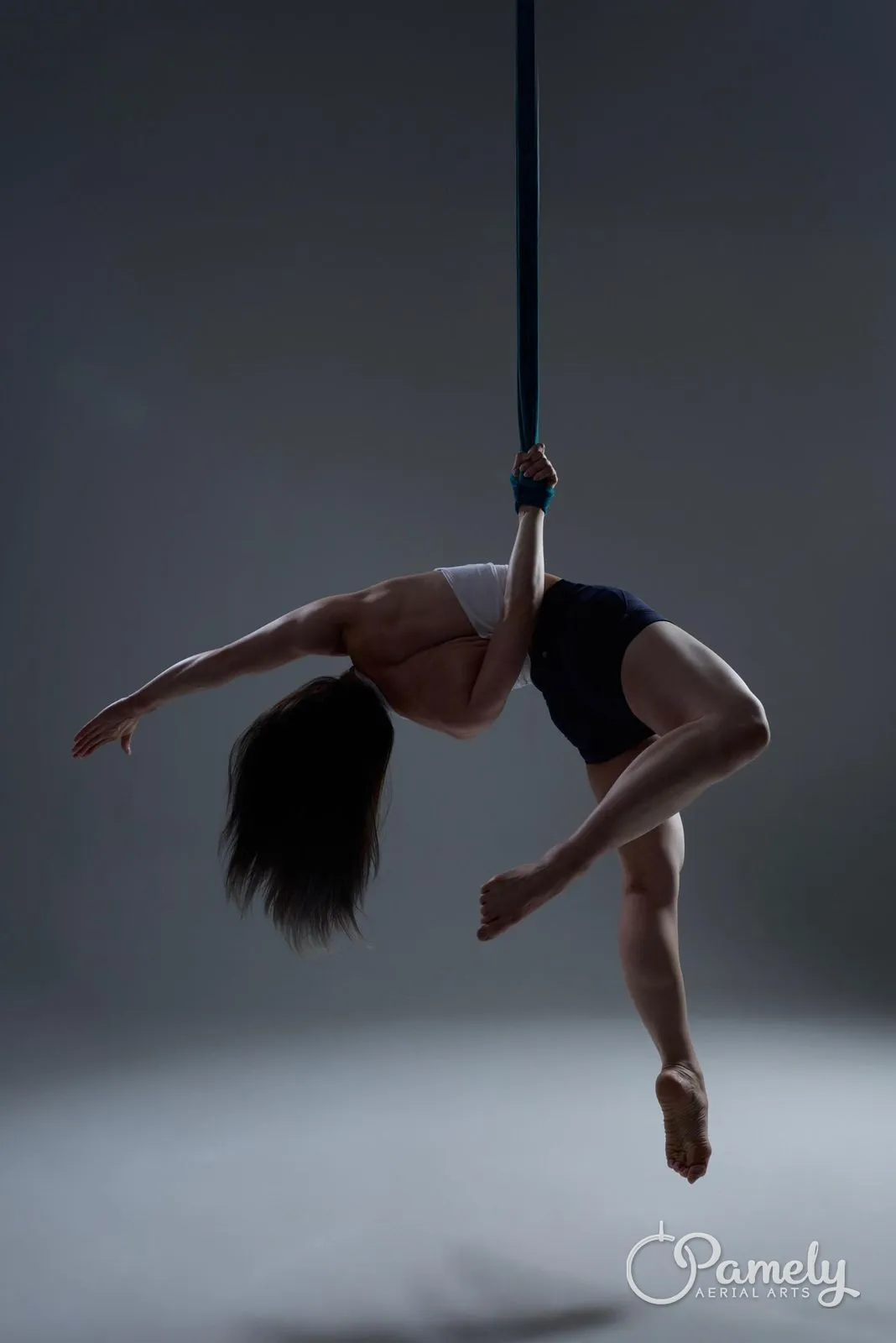 Pamely inverted on aerial straps against a grey backdrop